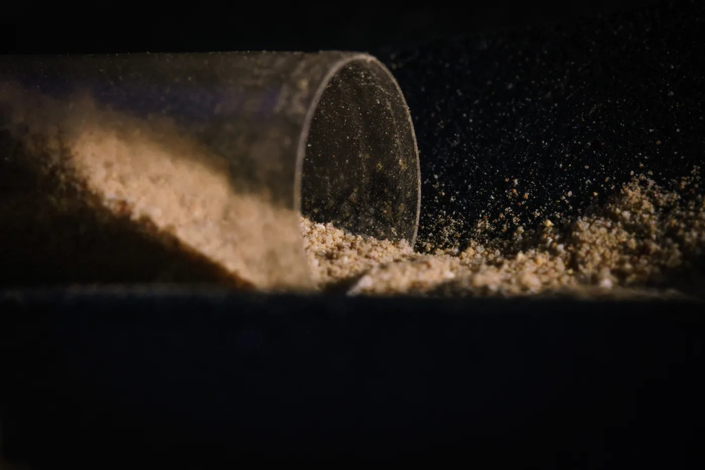 Makroaufnahme einer geöffneten Kapsel, aus der beiges Pulver auf dunklen Untergrund rieselt.